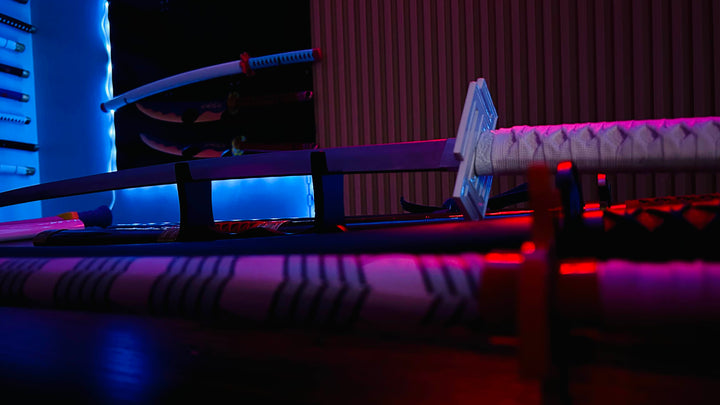 A collection of katanas rests on display stands under dramatic blue and red lighting, highlighting their sleek blades and wrapped handles in a modern, neon-lit setting.