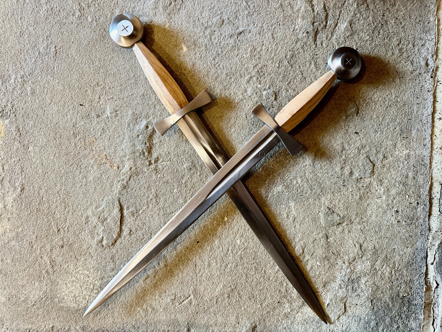 Crossed medieval daggers with wooden handles and metal pommels resting on a stone surface.
