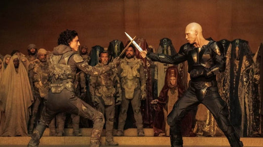 Two armored men engaged in a knife duel inside a grand hall, surrounded by onlookers in desert robes and military uniforms, facing each other with blades raised in a tense standoff.
