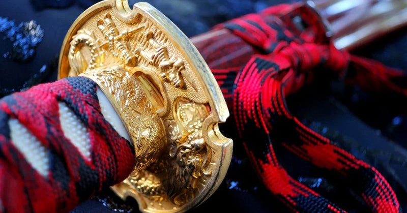 Close-up of a gold samurai sword guard with a red-and-black wrapped handle.