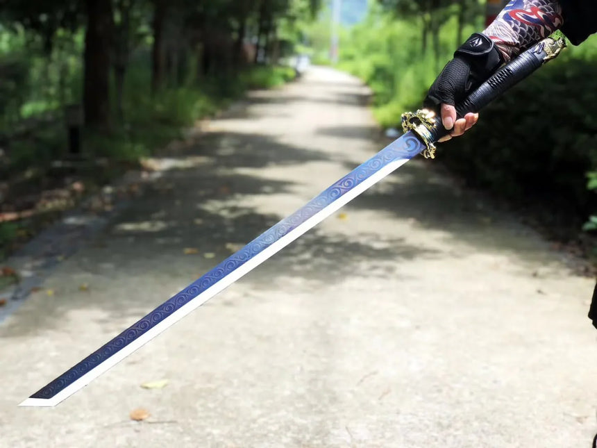A decorative katana-style sword with a deep blue engraved blade and ornate gold tsuba held outward along a tree-lined path, with intricate scroll patterns running the length of the blade.