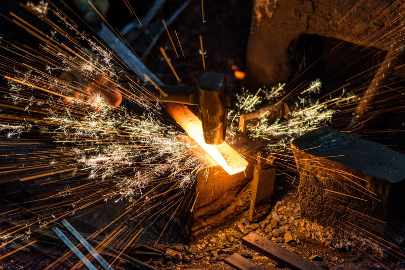 A blacksmith hammering glowing hot steel on an anvil, sending bright sparks flying in a dark forge.