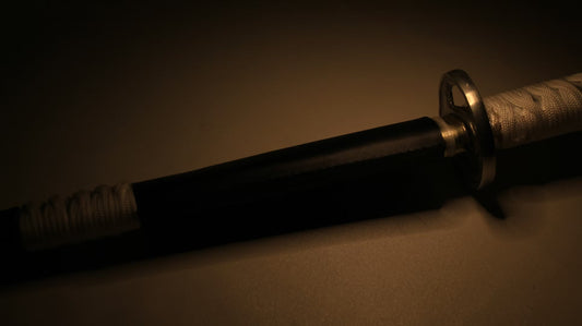 A dimly lit katana resting on a surface, featuring a black scabbard and a white-wrapped handle with a circular guard.