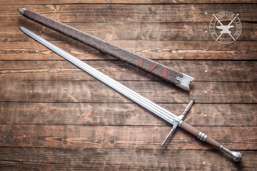 "Long medieval sword with a detailed hilt lying next to its leather-wrapped scabbard on a wooden surface."