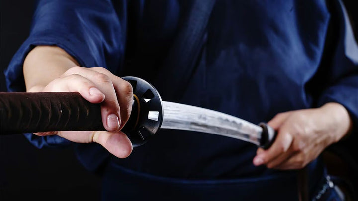 Person in blue clothing holding and drawing a katana sword.