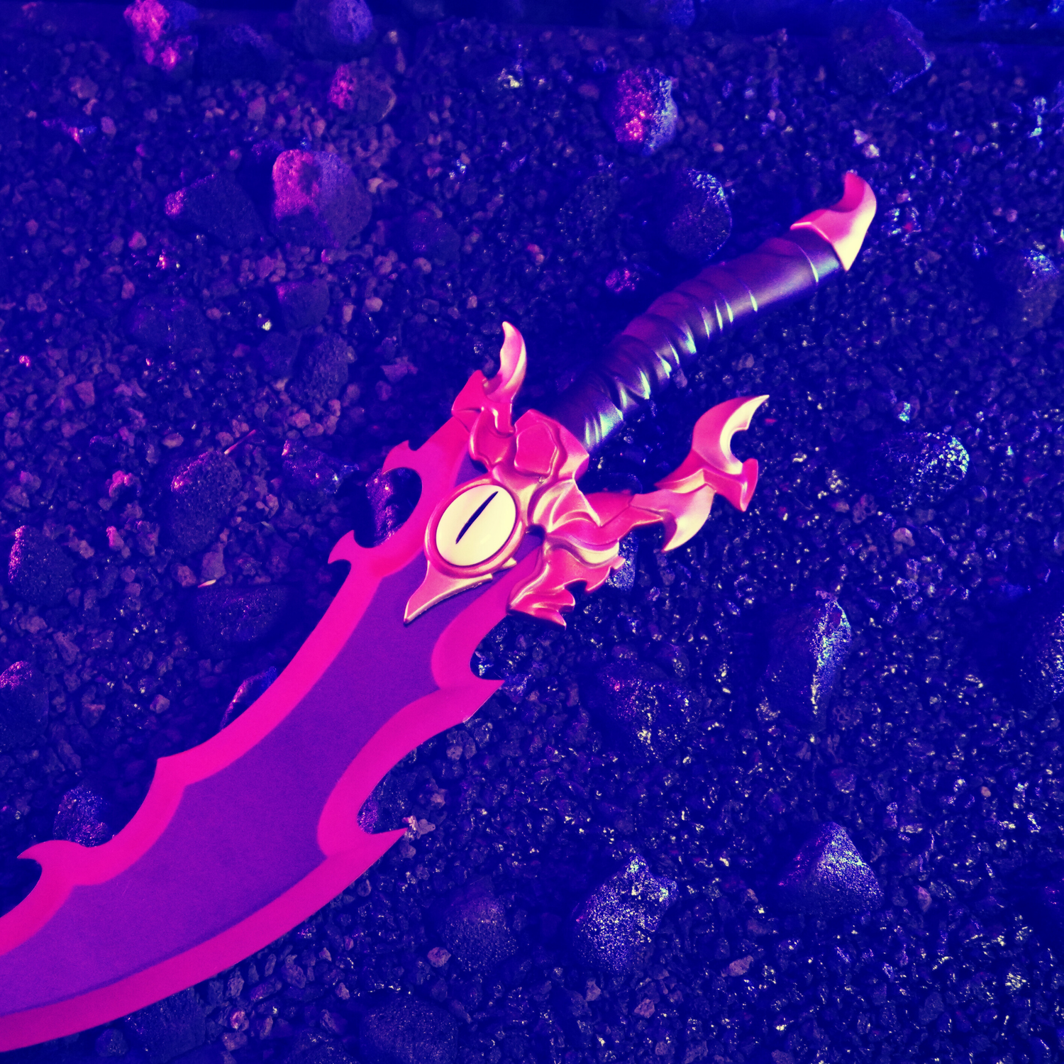 Purple fantasy sword with jagged blade and gold guard lying on dark gravel.
